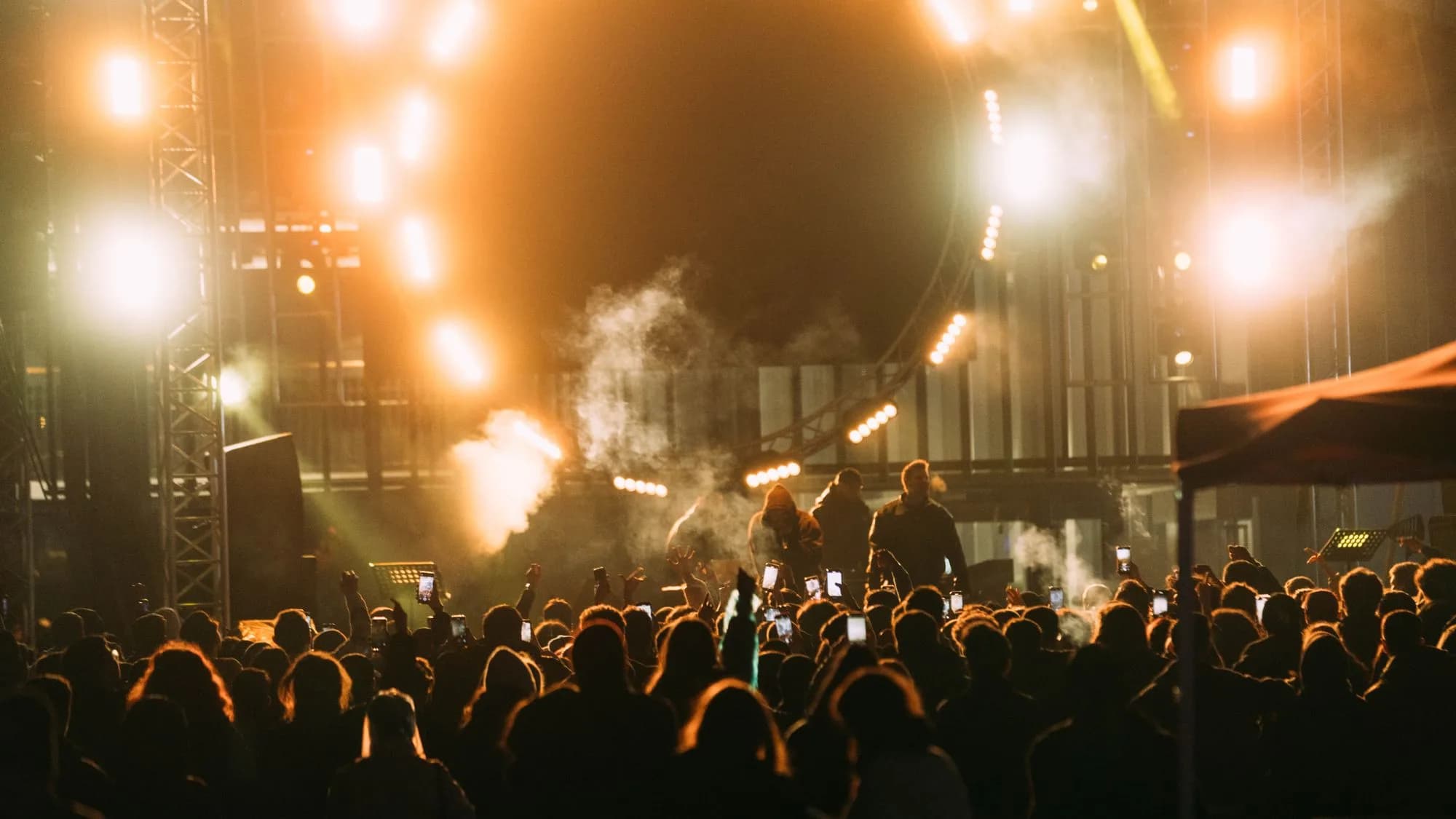 Large concert crowd facing a brightly illuminated production stage at night.