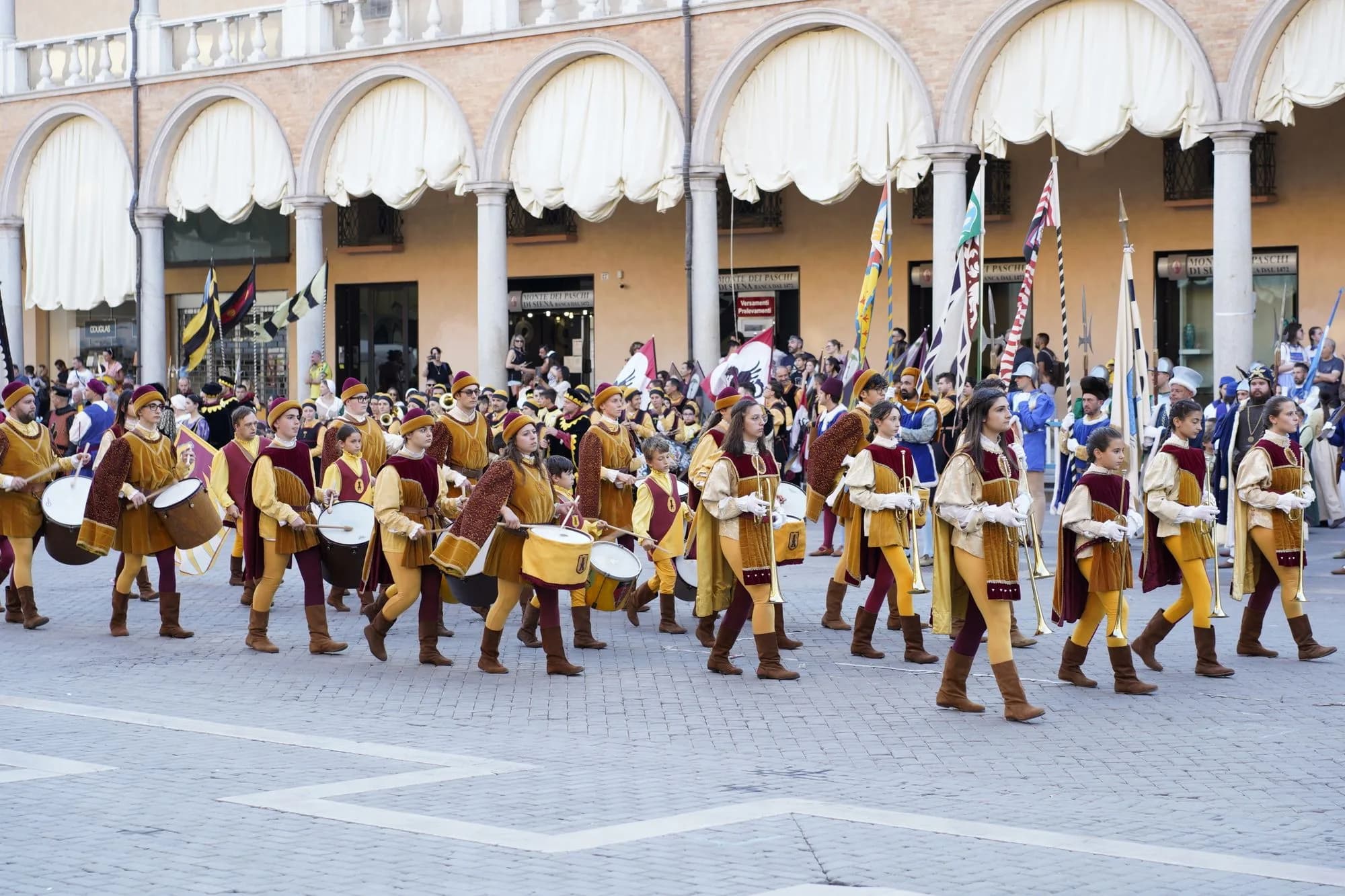 Festive Italian street procession with musicians, flags and a gathered crowd.