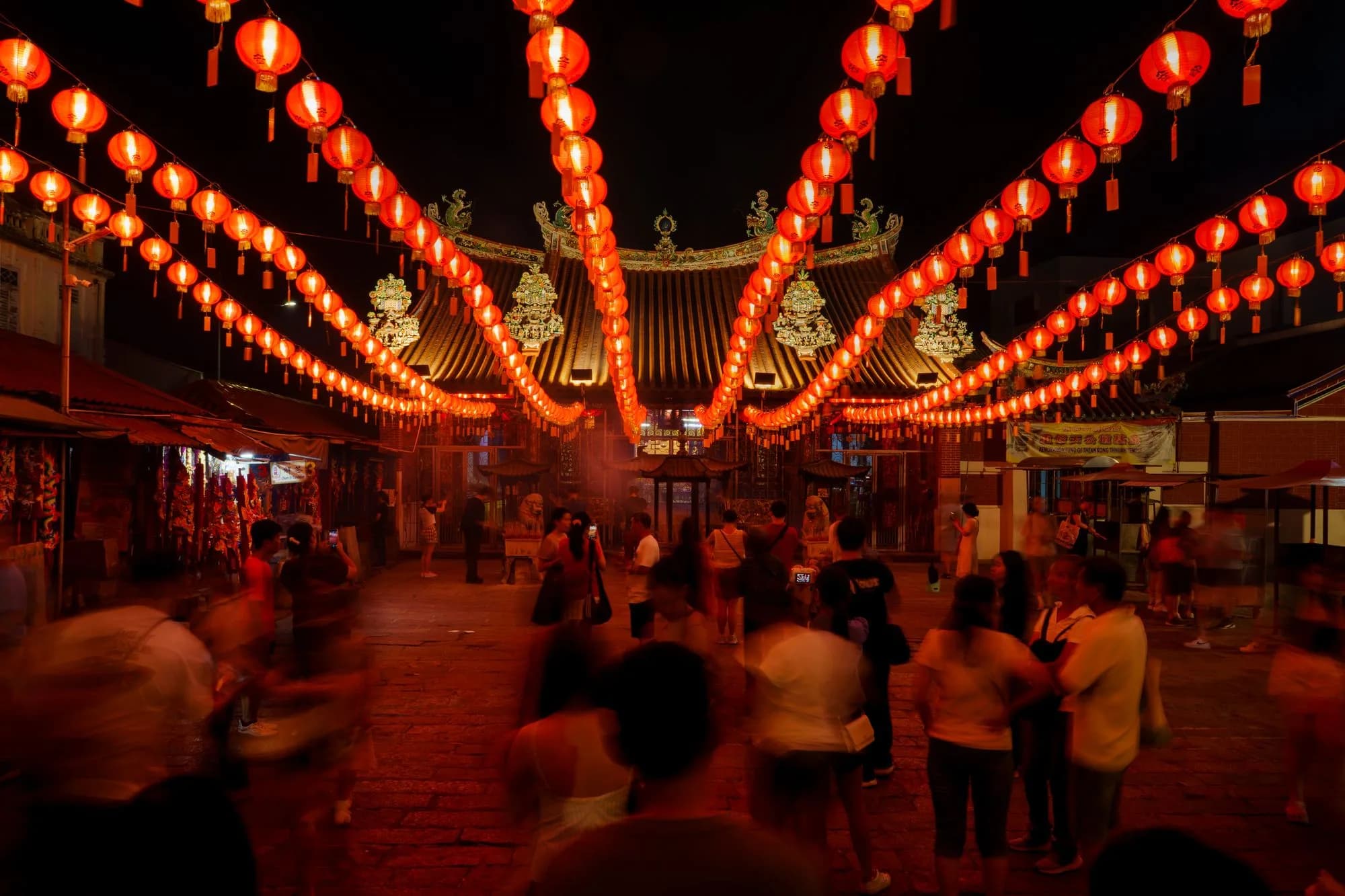 Crowd gathered beneath glowing red lanterns during a vibrant nighttime cultural festival.