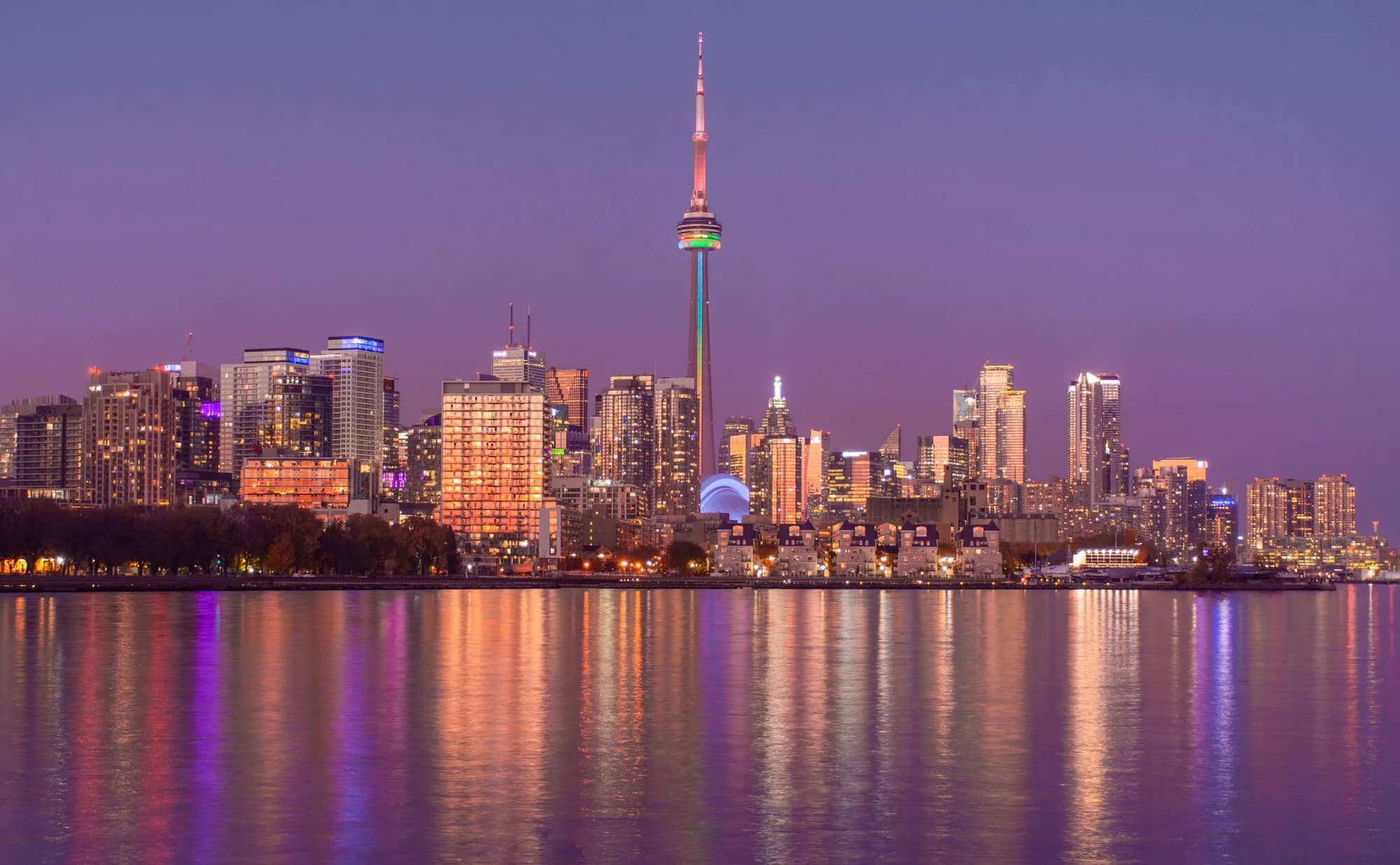 Toronto skyline illuminated at night and reflected across Lake Ontario.